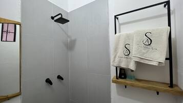 A shower area with a black handheld showerhead, a towel rack with two towels, and a wooden shelf with toiletries.