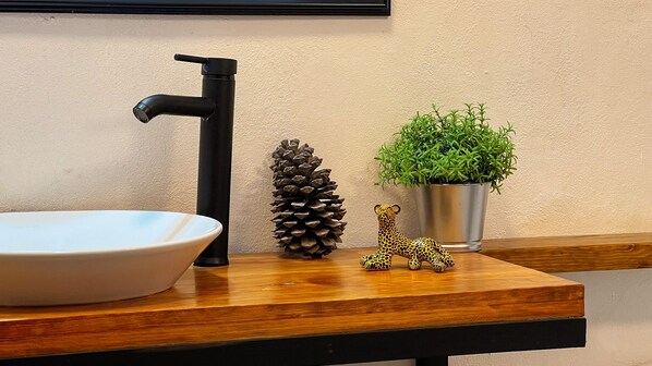 Un lavamanos con grifo negro, una piña, una figurita de jirafa pequeña y una planta en maceta sobre una encimera de madera.