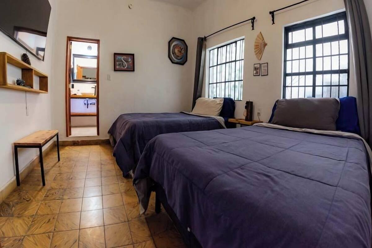 A bedroom with two beds, a wooden bench, a small table, and a window with a view.