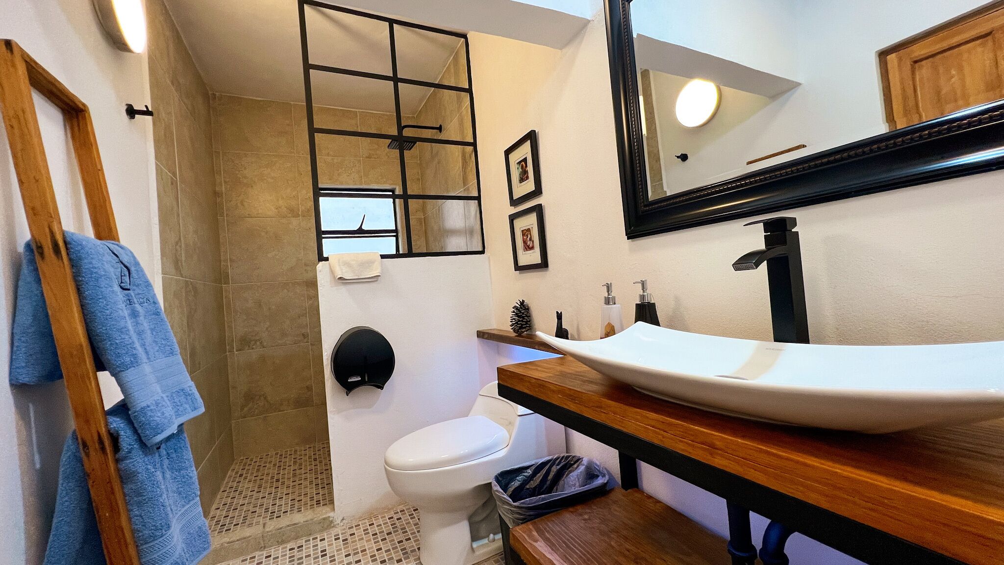 Un baño con tocador de madera, lavamanos blanco, inodoro y zona de ducha con puerta de cristal.