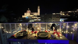 Mesa para comer dispuesta con platos, cubiertos y una copa, con vistas a un edificio histórico con un campanario de noche.