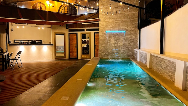Una piscina interior con caída de agua, suelo de madera y zona de bar con asientos.