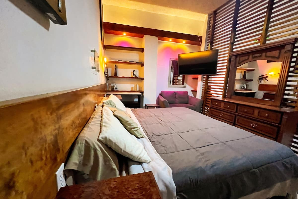 A hotel room with a large bed, a wooden headboard, a television mounted on the wall, and a wooden dresser.