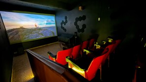 A cinema room with a large screen, red seating, and a dark wall with geometric patterns.