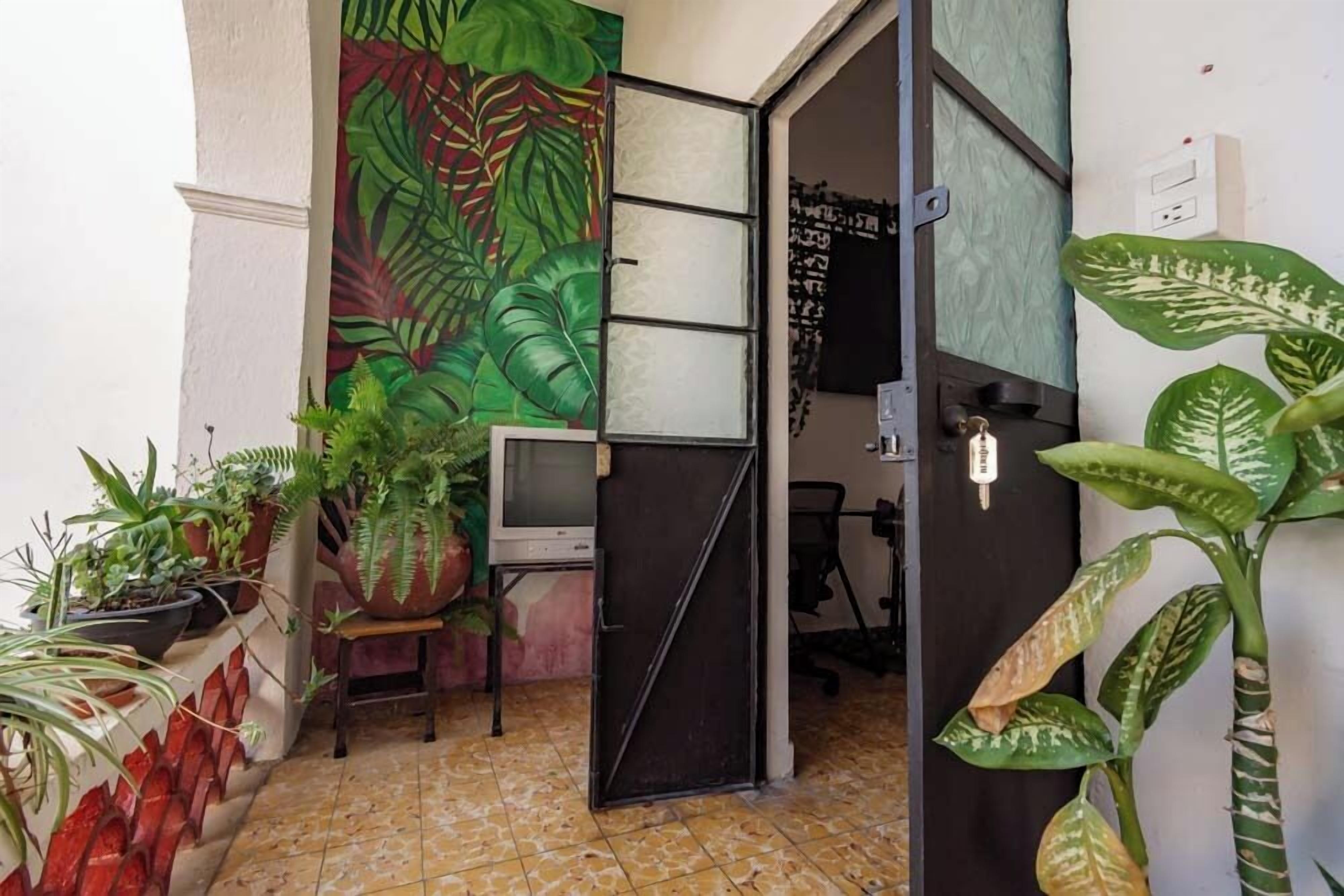 Un petit bureau avec un sol carrelé, un bureau, une chaise et une grande fresque murale représentant des feuilles vertes.