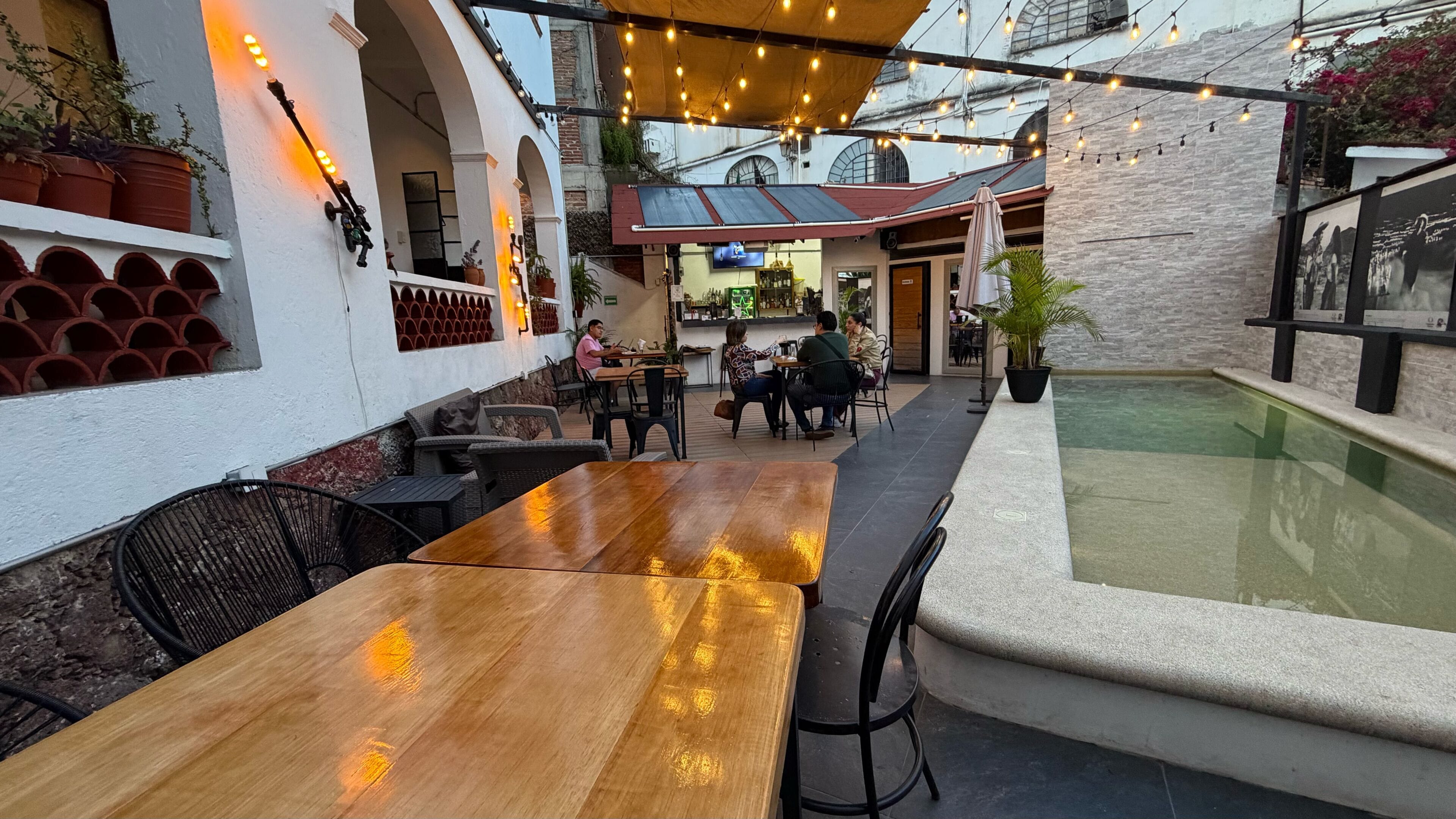 Een buitenzitgedeelte met tafels en stoelen, een zwembad en een bar met een televisie.