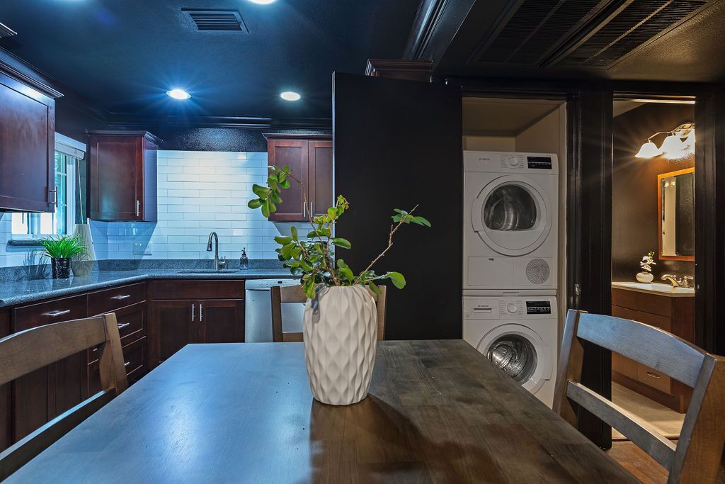 Une cuisine moderne avec des meubles en bois foncé, un mur de briques blanches et un lave-linge encastré.