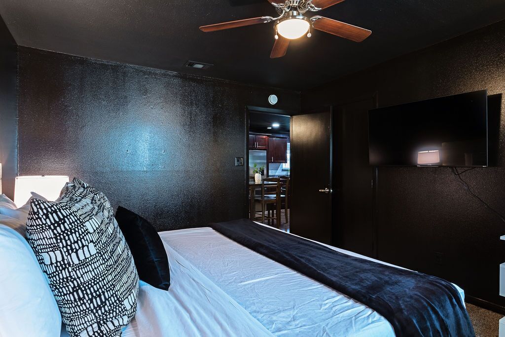 Une chambre d’hôtel équipée d’un lit, d’un ventilateur de plafond, d’un téléviseur fixé au mur et d’une porte donnant sur un coin cuisine.