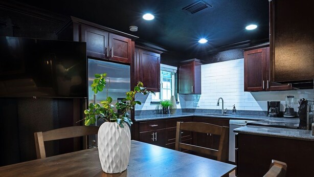 Una cocina moderna con armarios de madera oscura, electrodomésticos de acero inoxidable y una mesa de comedor de madera con un jarrón blanco.