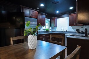 Une cuisine moderne avec des meubles de couleur bois foncé, des appareils en acier inoxydable et une table à manger en bois sur laquelle est posé un vase blanc.