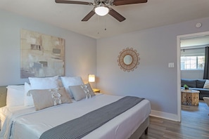 Un dormitorio con cama, ventilador de techo, obra de arte, espejo decorativo y vistas a un salón.