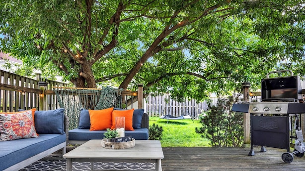 Une terrasse extérieure avec une plateforme en bois, un canapé bleu avec des coussins orange, une table basse avec un plateau en osier et un barbecue.