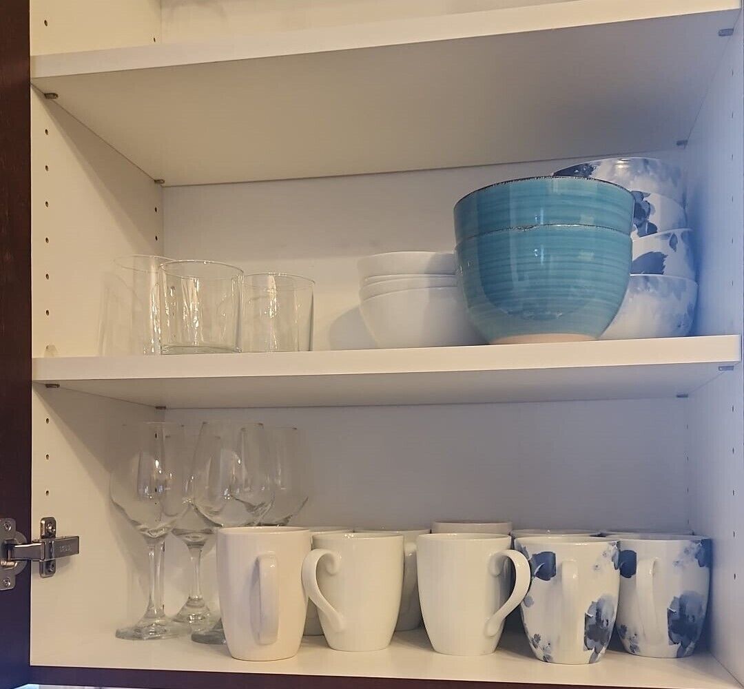 A white shelf unit with clear glass cups, white mugs, and a blue bowl.