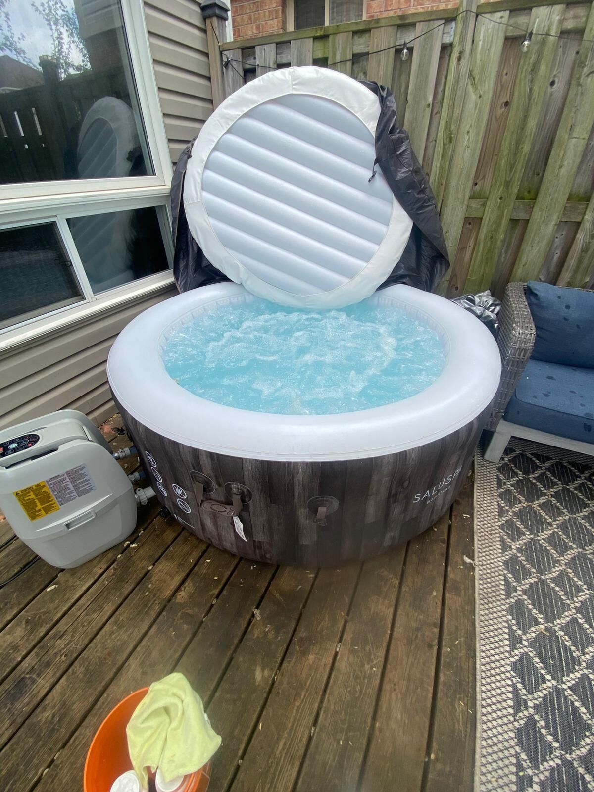 A hot tub with a control panel and a gas tank on a wooden deck.