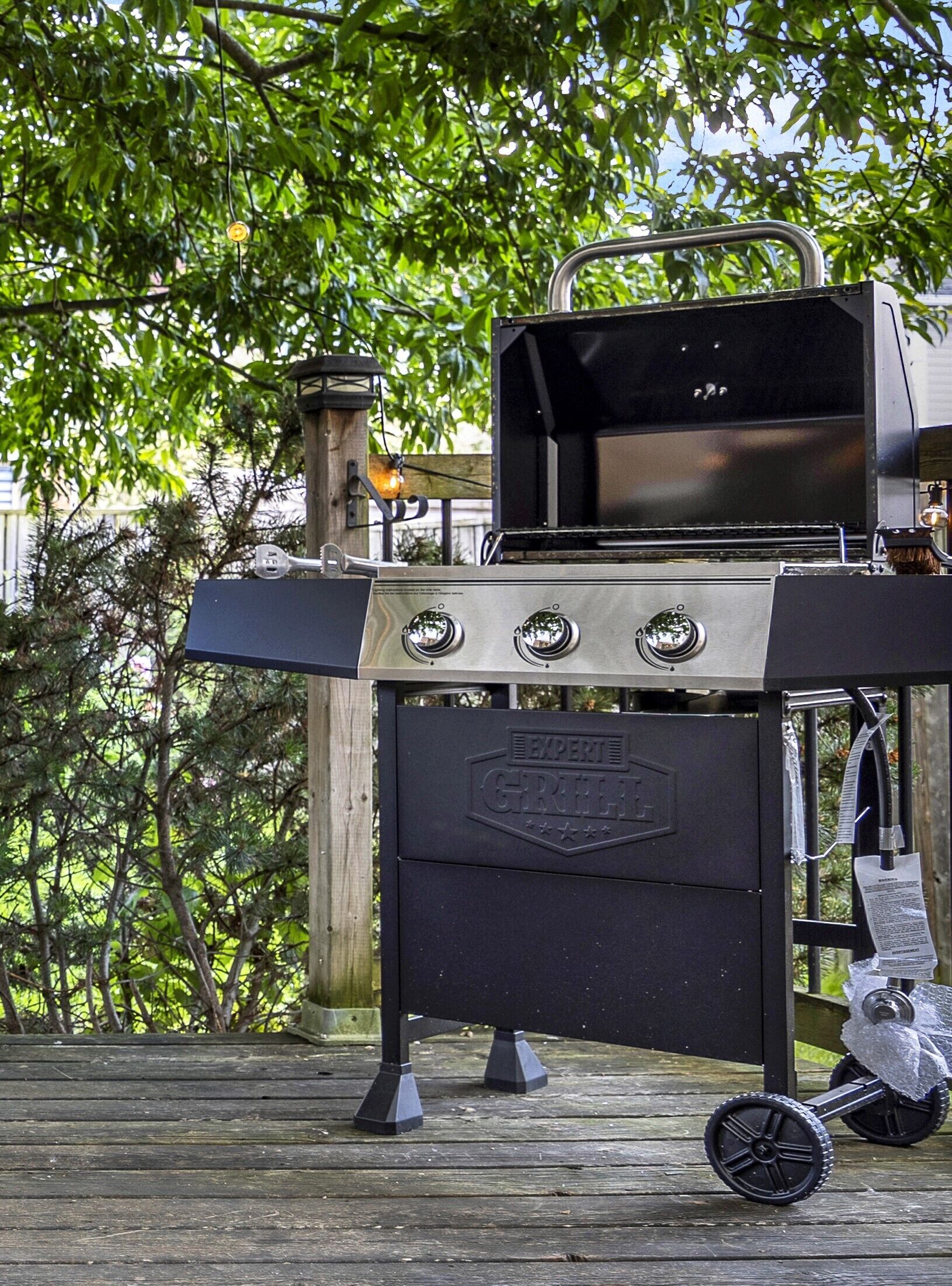Una parrilla portátil con tres quemadores y una chimenea, ubicada en una terraza de madera.