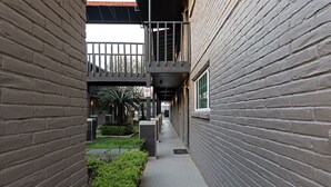 A narrow brick corridor with a concrete path, a small garden area, and a balcony with a metal railing.