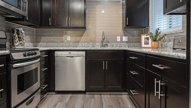 A modern kitchen with dark cabinetry, a stainless steel stove, a dishwasher, and granite countertops.