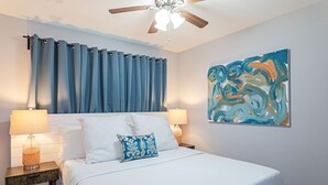 A bedroom with a bed, two bedside tables, a ceiling fan, and a wall-mounted abstract painting.