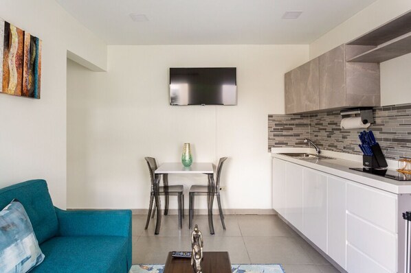 A modern kitchen with a flat-screen TV, a dining table with chairs, and a sofa. - Emerald 1BR APT -#E3 in Noord-Sleeps 2 (Noord)