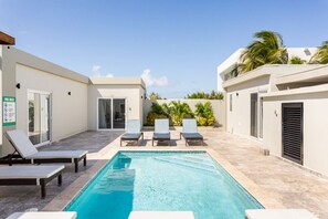 A swimming pool with lounge chairs, a sign indicating a pool area, and a building with a door and windows. - Emerald 1BR APT -#E3 in Noord-Sleeps 2 (Noord)
