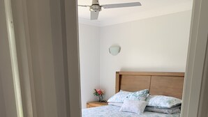 A bedroom with a bed, a nightstand, a wall clock, and a ceiling fan.