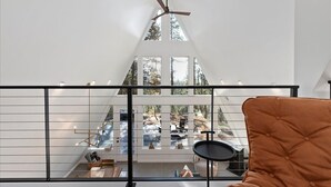 Een modern interieur met een balkon met glaspanelen, een plafondventilator en uitzicht op een bebost gebied.