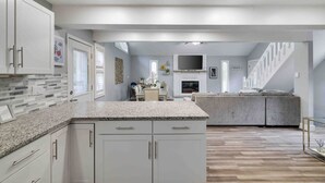 A modern kitchen with white cabinetry, granite countertops, and a built-in fireplace. - Modern Poconos Central Cozy 5BR Home - Game Room (Tobyhanna)