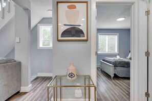 Um interior moderno com escada, uma obra de arte abstrata emoldurada, um vaso decorativo e um vislumbre de um quarto com cama e janela.