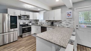 A modern kitchen with stainless steel appliances, white cabinetry, and a granite countertop. - Modern Poconos Central Cozy 5BR Home - Game Room (Tobyhanna)