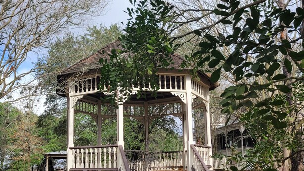 Ein Kiosk mit weiß-brauner Farbgebung, umgeben von Bäumen und einem Garten.