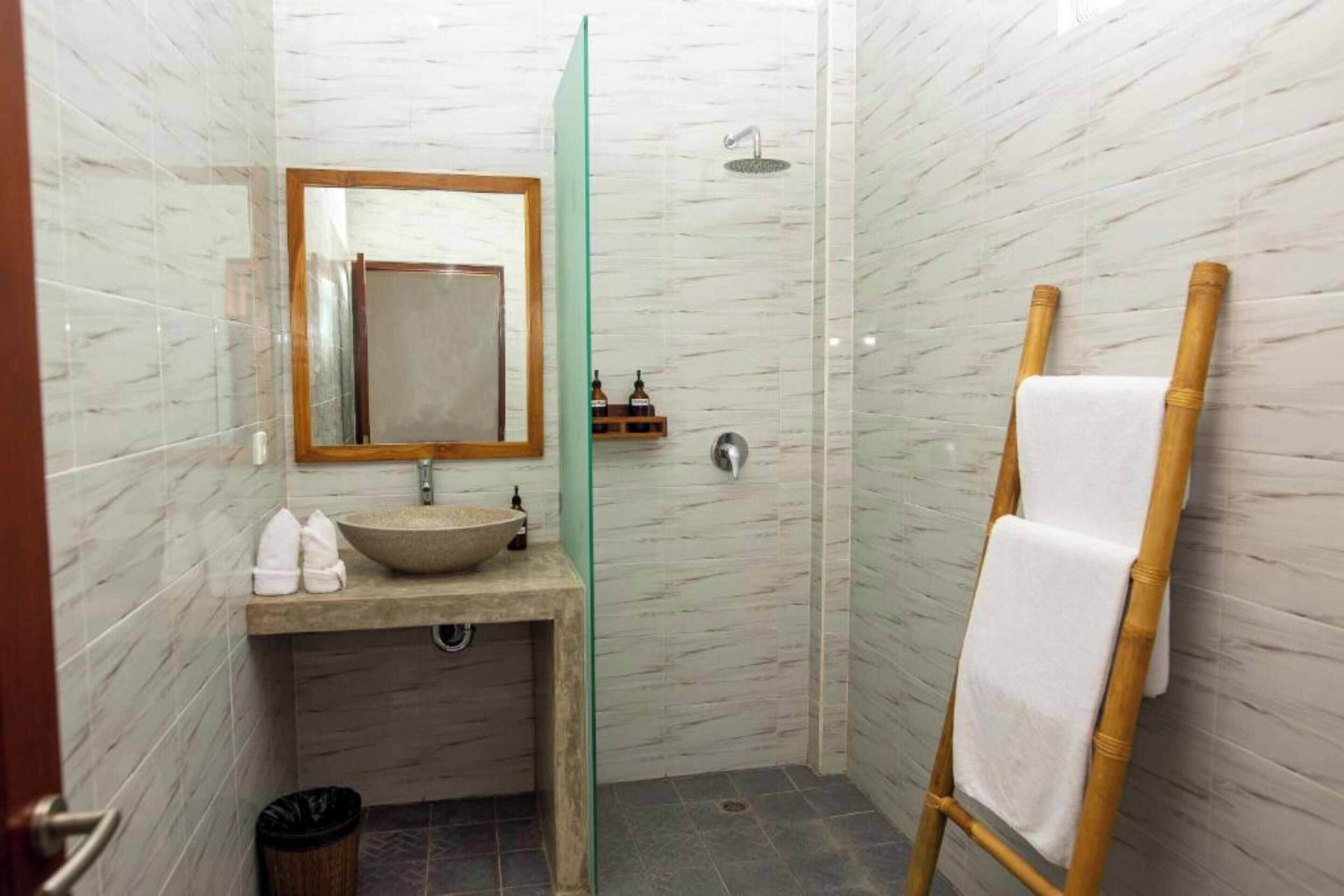 Ein Badezimmer mit Marmorwand, einem spiegel mit Holzrahmen, einem Waschbecken, einer Dusche und einem Handtuchhalter.