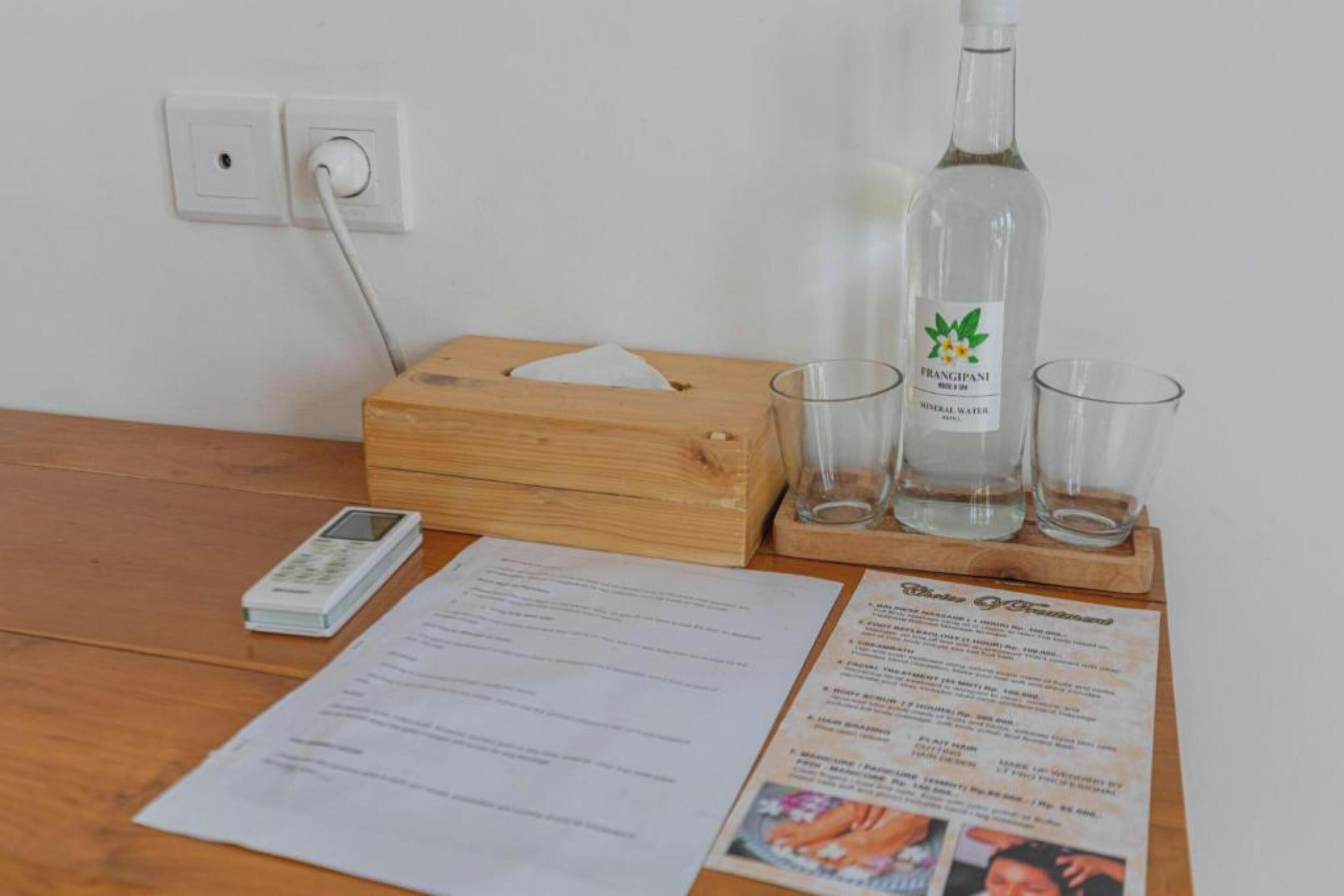 A wooden table with a tissue box, a mobile phone, a bottle of mineral water, and glasses.