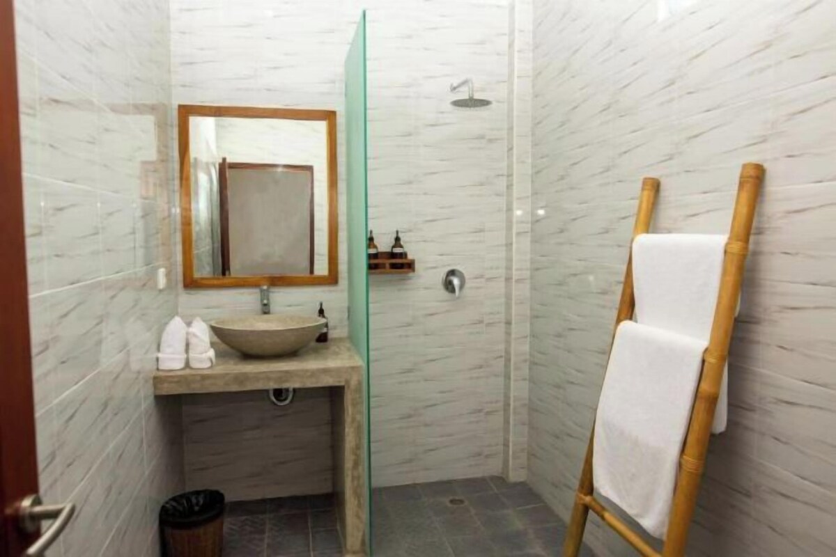 A bathroom with a marble wall, a wooden vanity with a bowl sink, a mirror, and a shower area.