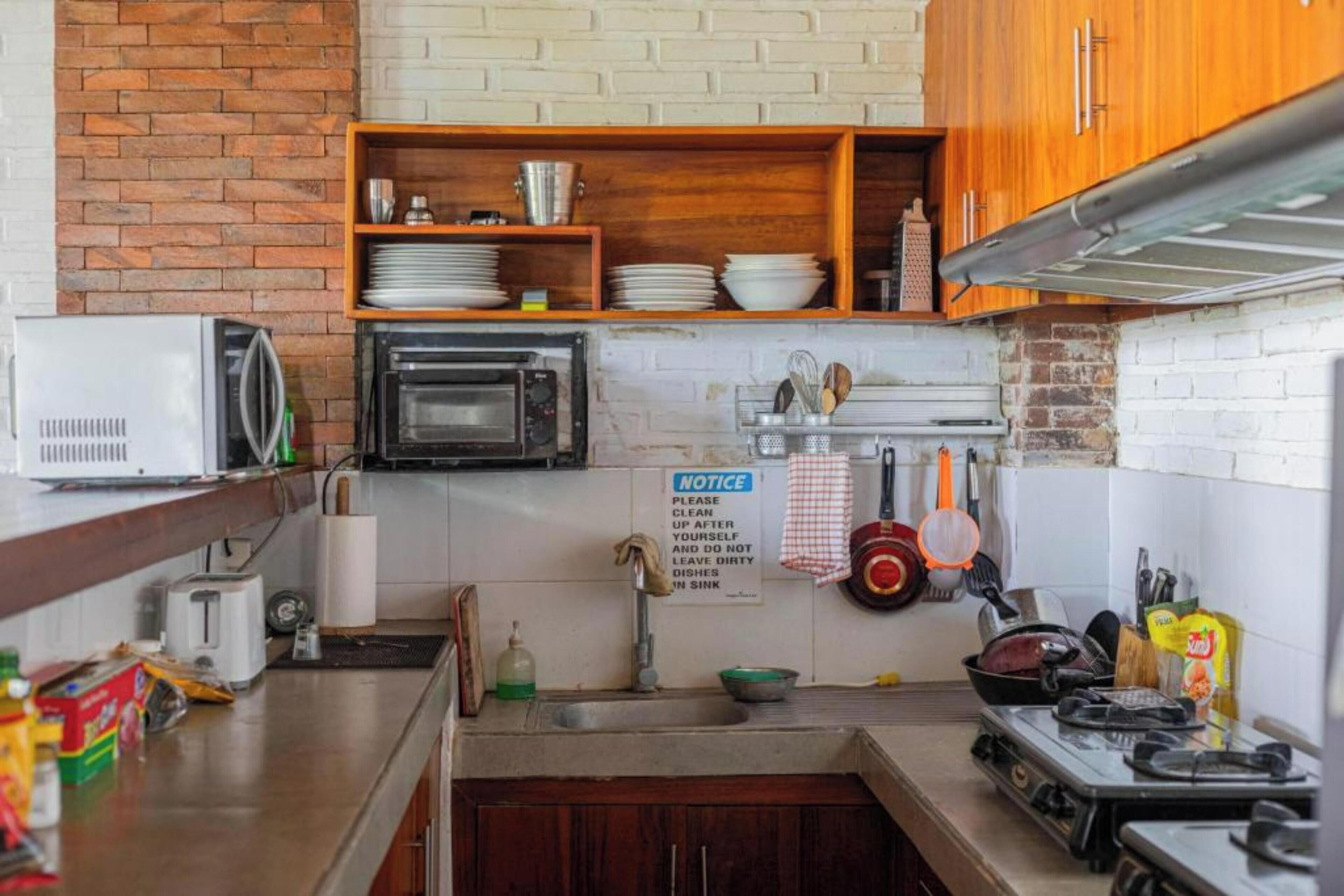 A kitchen with a brick wall, wooden cabinets, a microwave, an oven, a sink, and various kitchen utensils.