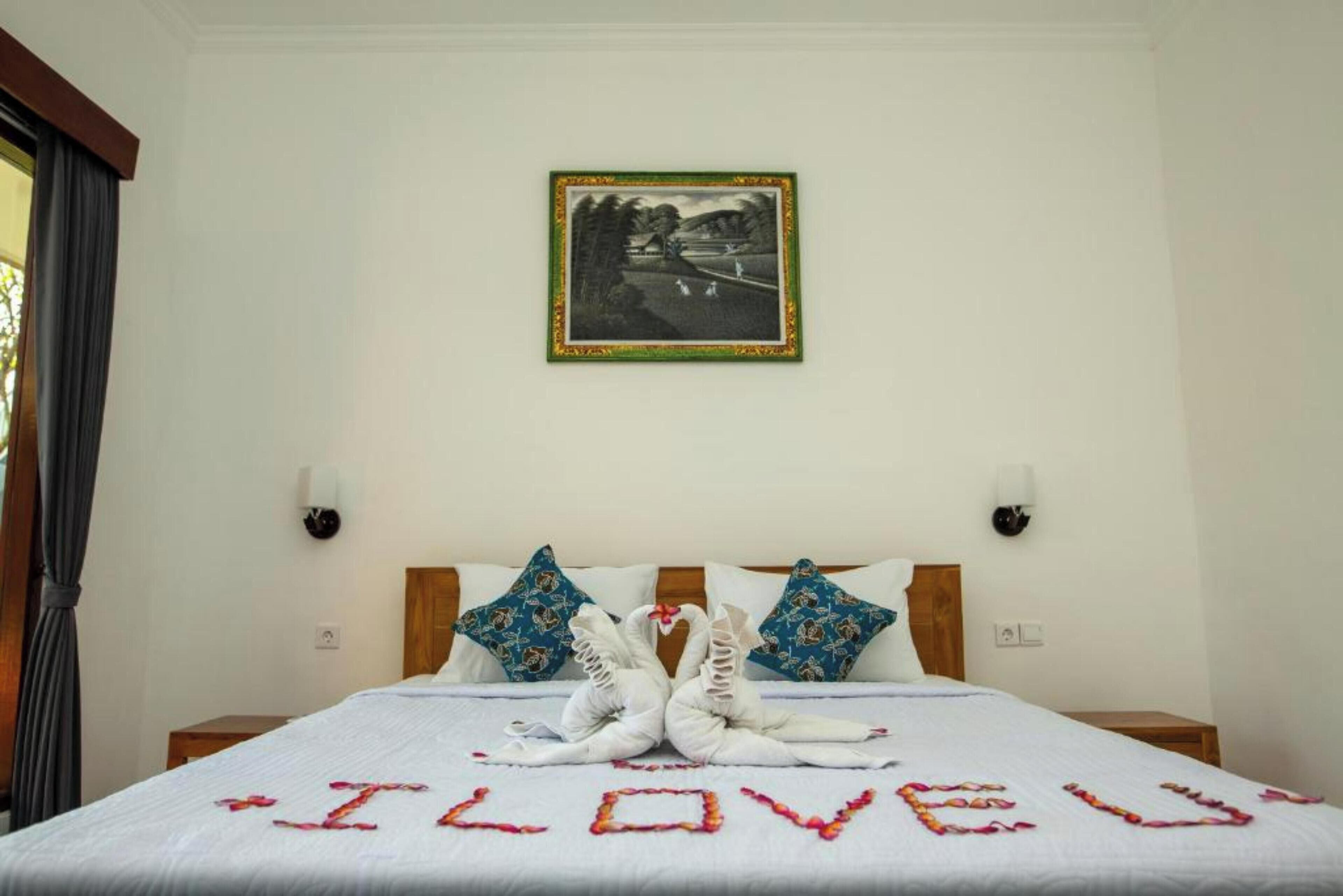 A hotel room with a bed, two decorative swans on the bed, and a framed picture on the wall.