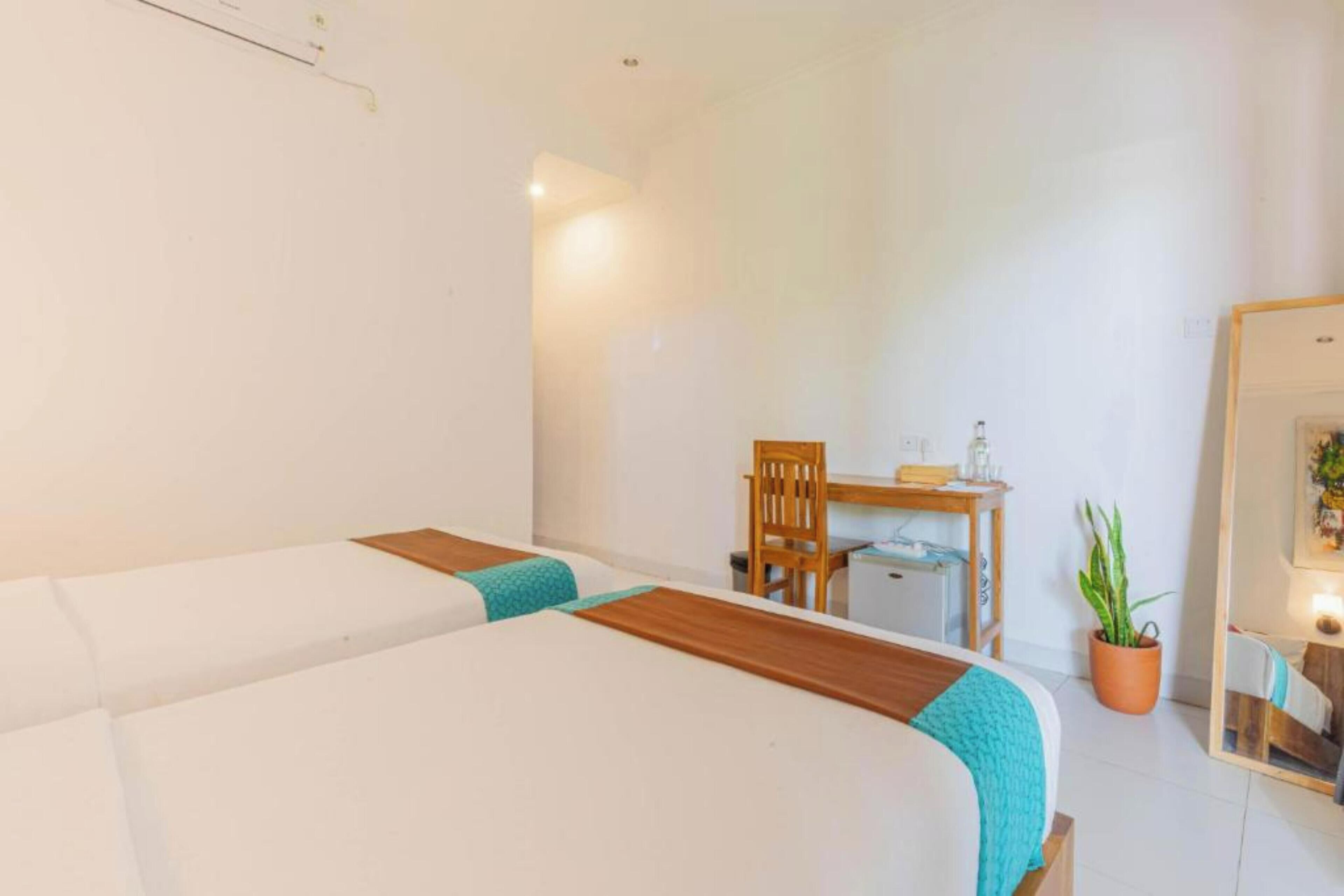 Habitación de hotel con dos camas, un escritorio, una silla, una planta en maceta y un espejo.