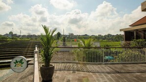 Una terraza con una planta en maceta, un letrero que dice 'FRANGIPANI' y vistas de un área ajardinada con una valla.