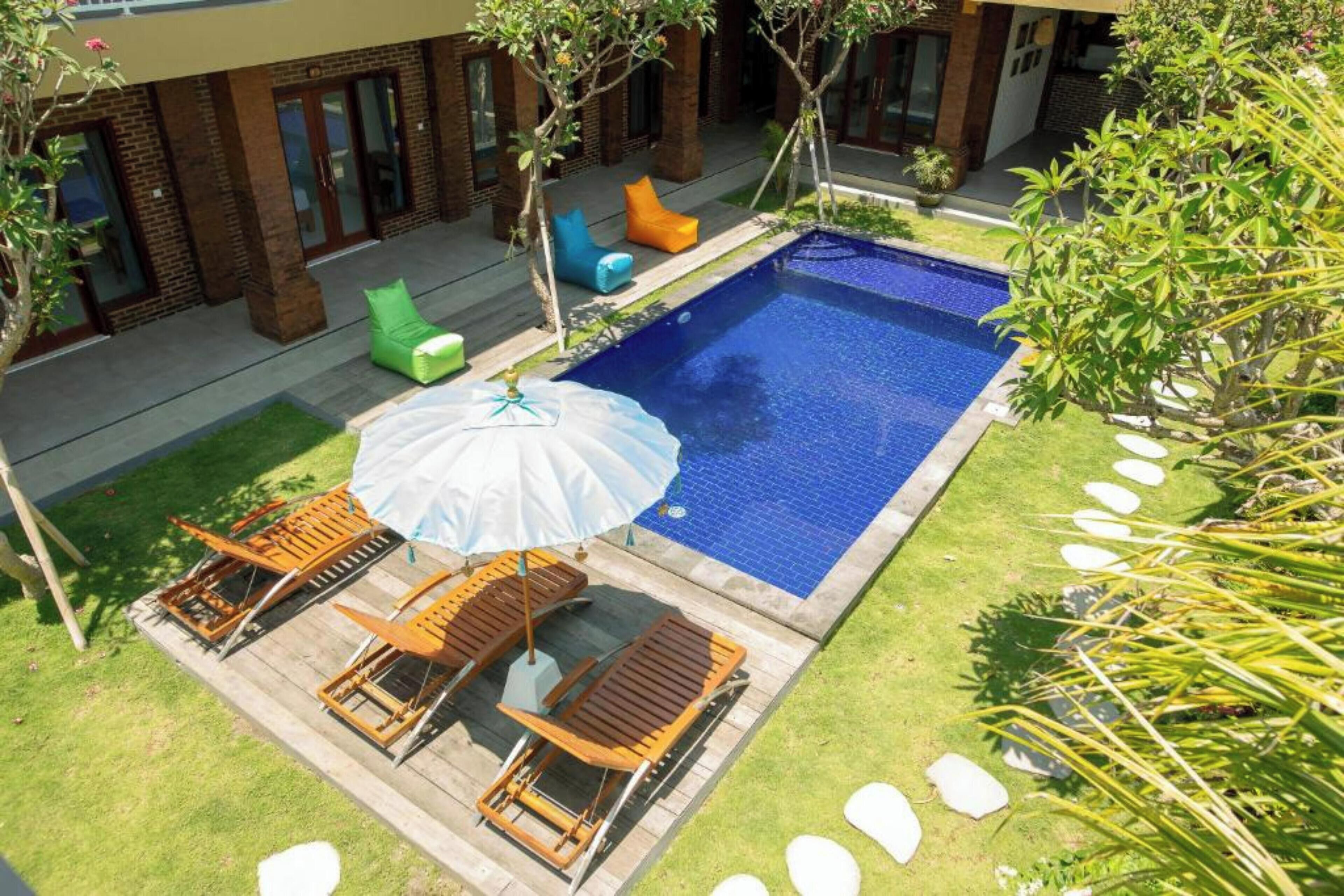 Ein Swimmingpool mit Liegestühlen und Sonnenschirm, umgeben von einem Backsteinhaus und Grünflächen.