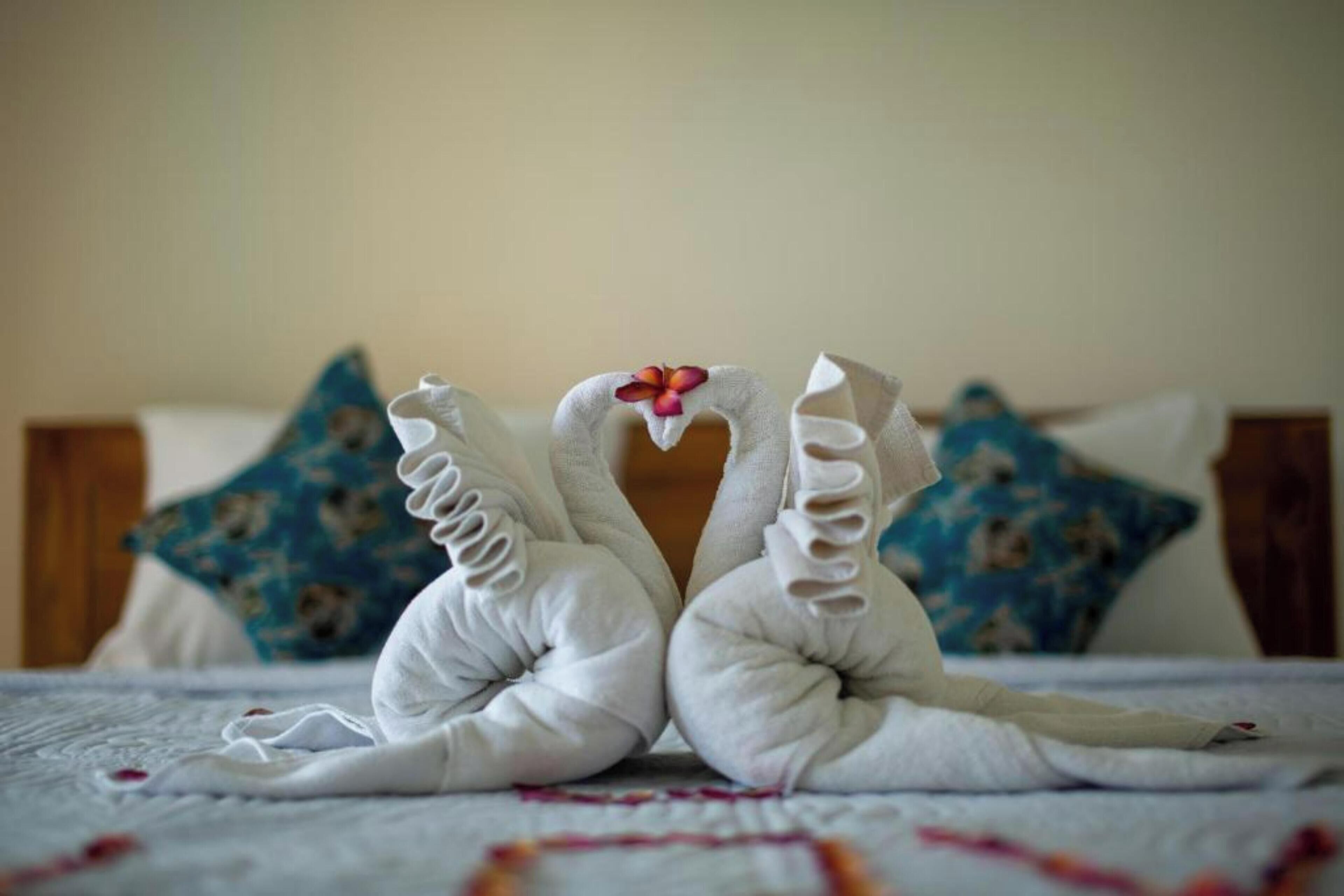 A bed with a white bedspread and two decorative swans made of towels.