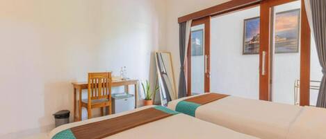 A hotel room with two beds, a desk, a chair, a small table, a trash bin, and a sliding glass door leading to a balcony.