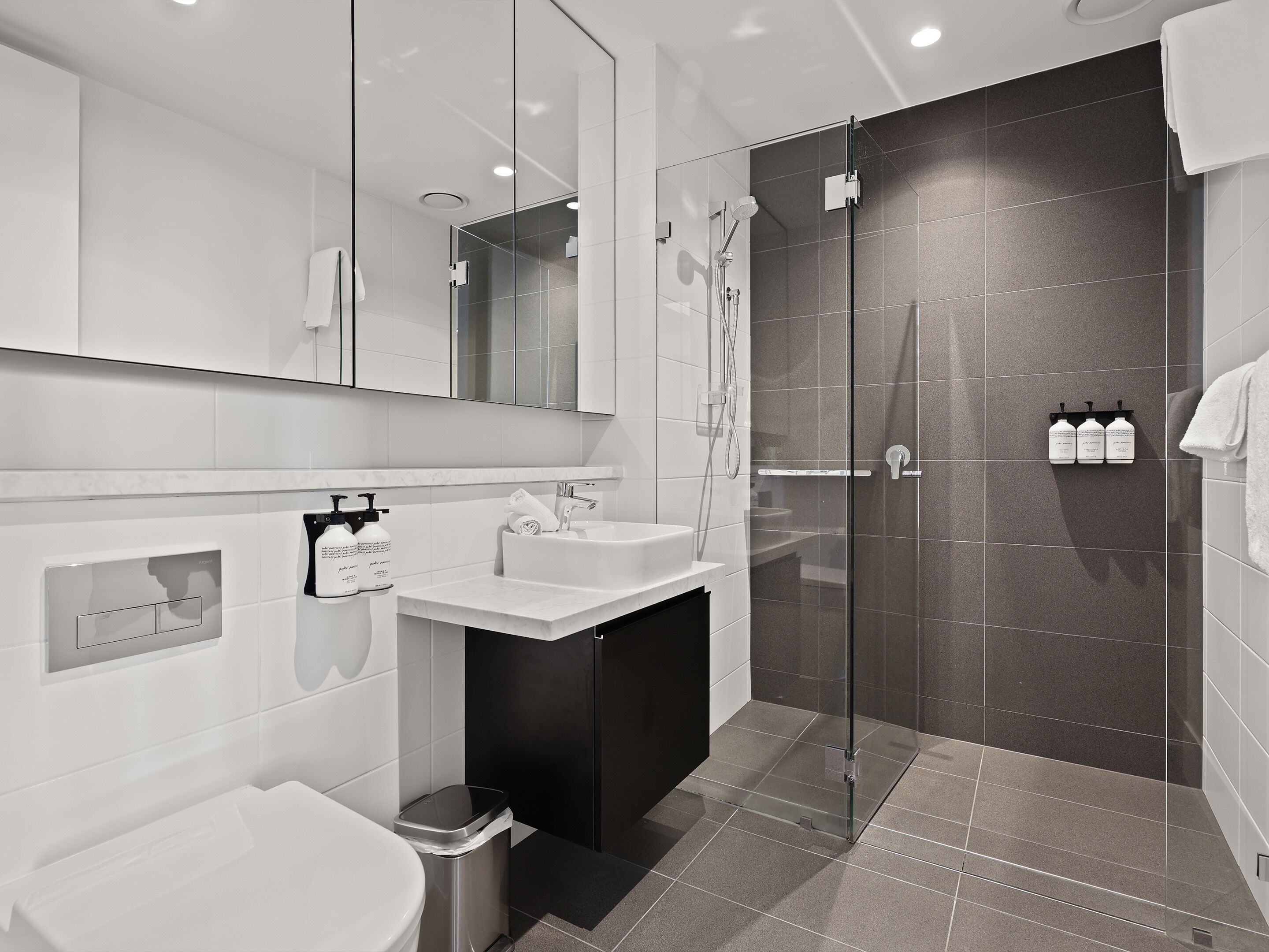 Un baño moderno con ducha envuelta en vidrio, un lavabo blanco y un espejo grande.