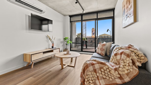 A modern living room with a sofa, a round coffee table, and a TV mounted on the wall. - Rambla @ Solarino House (Brunswick)
