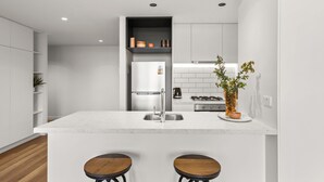 A modern kitchen with a central island, two stools, a built-in oven, and a potted plant. - Rambla @ Solarino House (Brunswick)