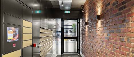 Un couloir avec un mur en briques, une grille métallique et un écran numérique sur le côté gauche.