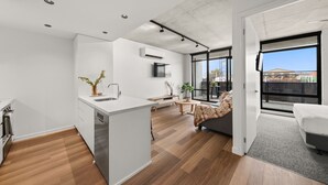 A modern kitchen with a central island, a dining area with a bench, and a large window offering a view of the outdoors. - Rambla @ Solarino House (Brunswick)