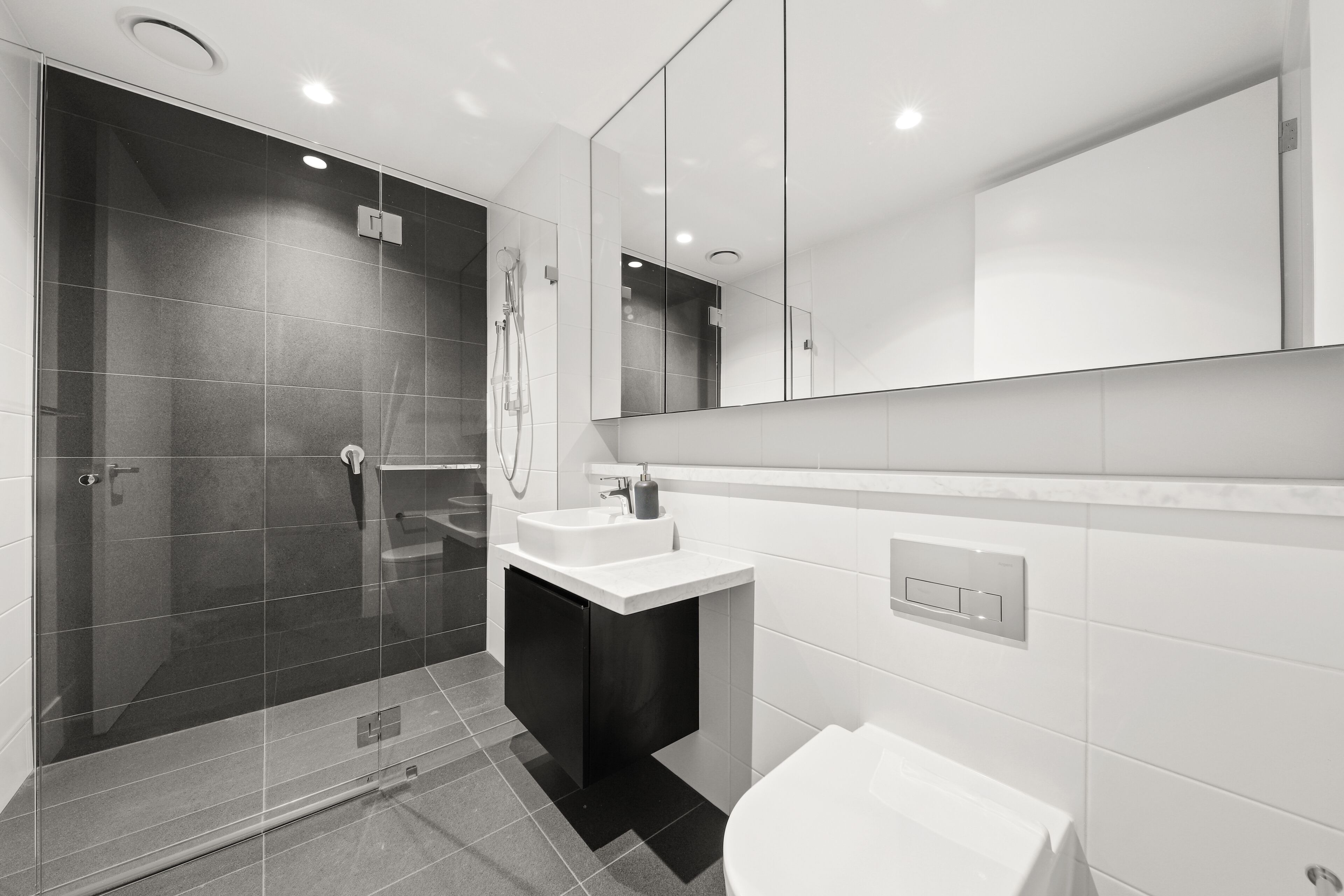 A modern bathroom with a glass-enclosed shower, a white sink, and a large mirror.