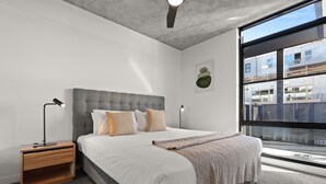 A modern bedroom with a large bed, two bedside tables, a ceiling fan, and a view of the city through large windows. - Rambla @ Solarino House (Brunswick)