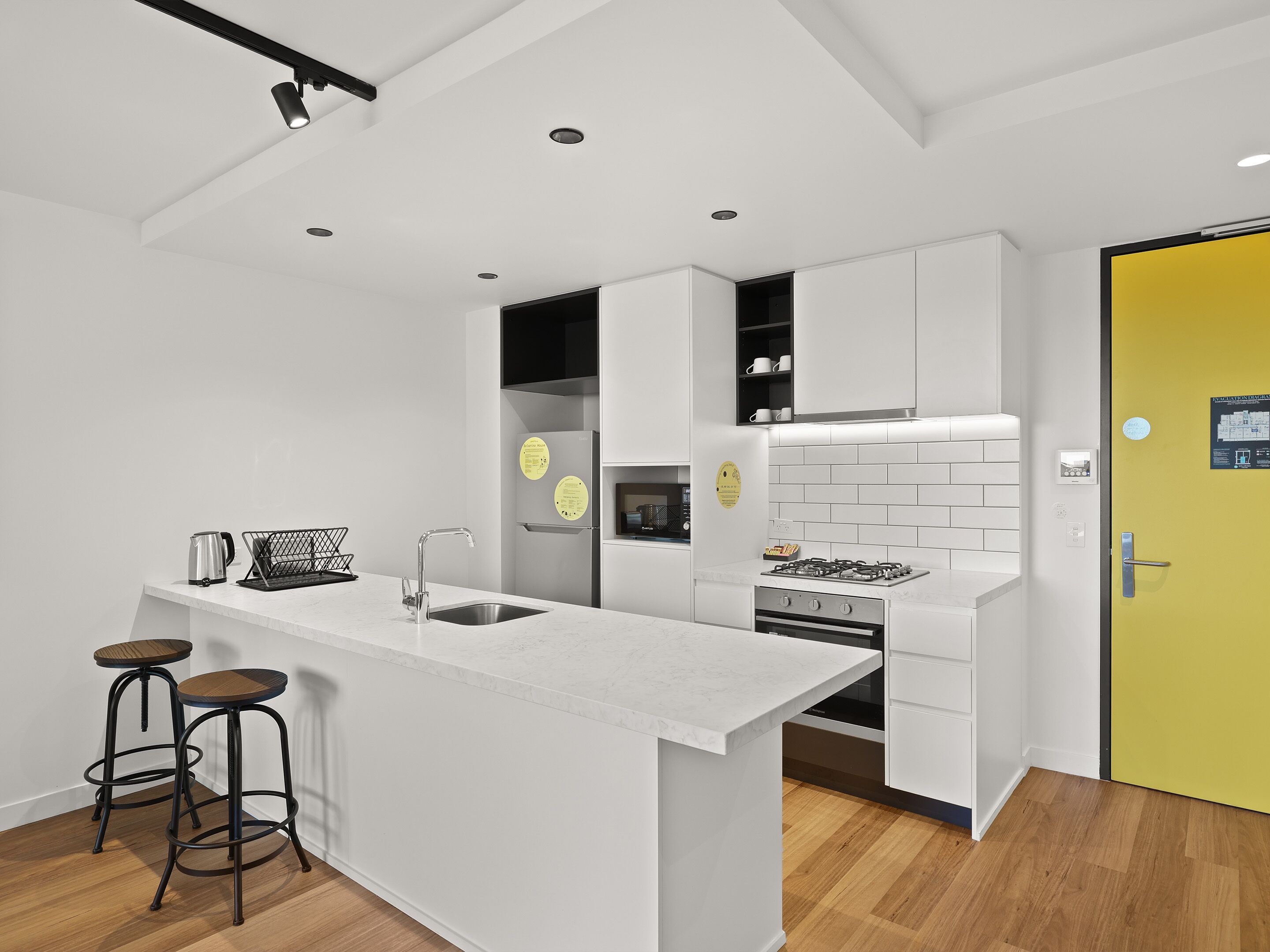 A modern kitchen with white cabinetry, a central island with stools, a yellow door, and a visible stove.