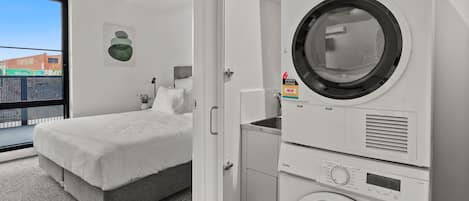 A compact laundry room with a built-in washer and dryer, a grey bed, and a ceiling fan.