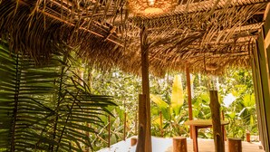 A thatched roof structure with wooden furniture and lush greenery. - Awaken Yoga Eco Resort in Amazon jungle (Indiana)
